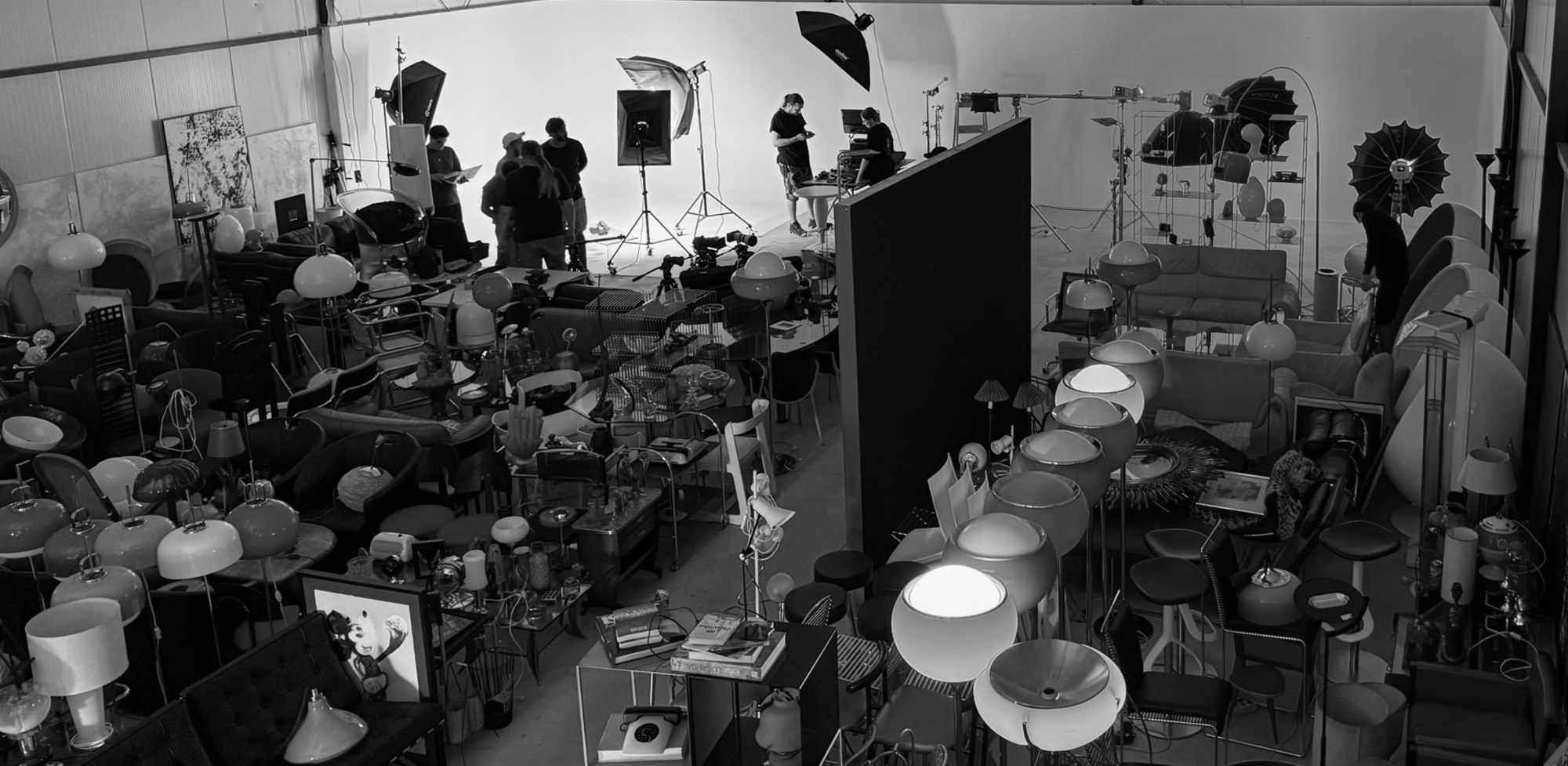 The Studio SPACE prop hall seen from above — rows of vintage globe lamps, sofas and chairs, with a crew shooting against the white cyc at the far end