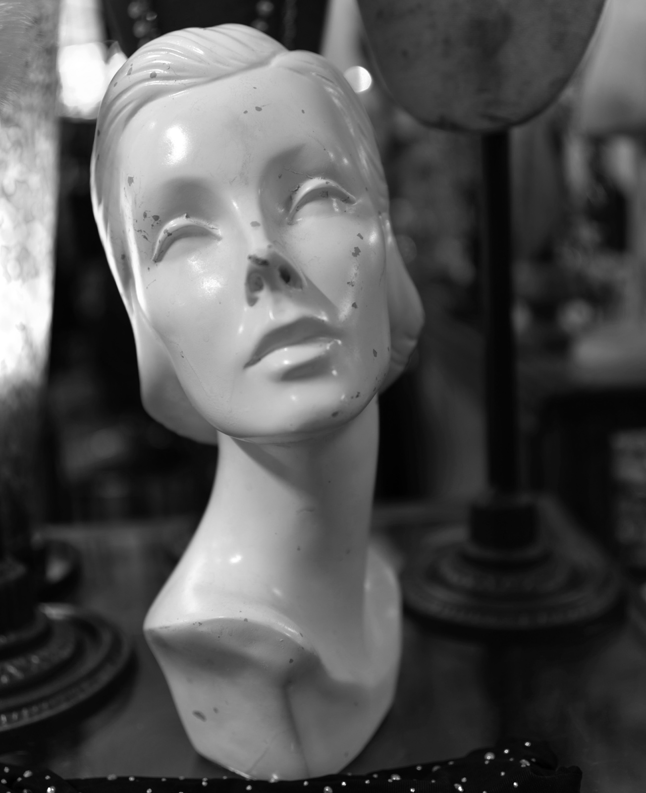 A chipped white mannequin head tilted back among lamp bases in the prop archive