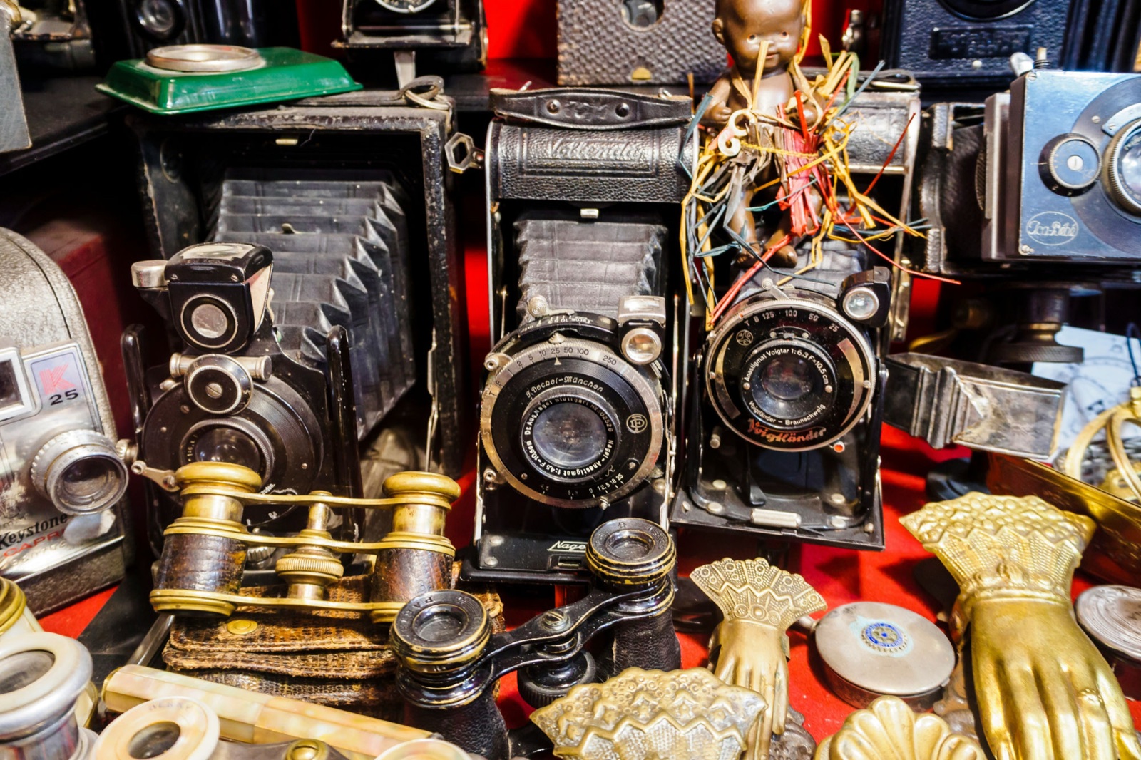 Antique folding bellows cameras, brass opera glasses and gilded hands laid out on red velvet